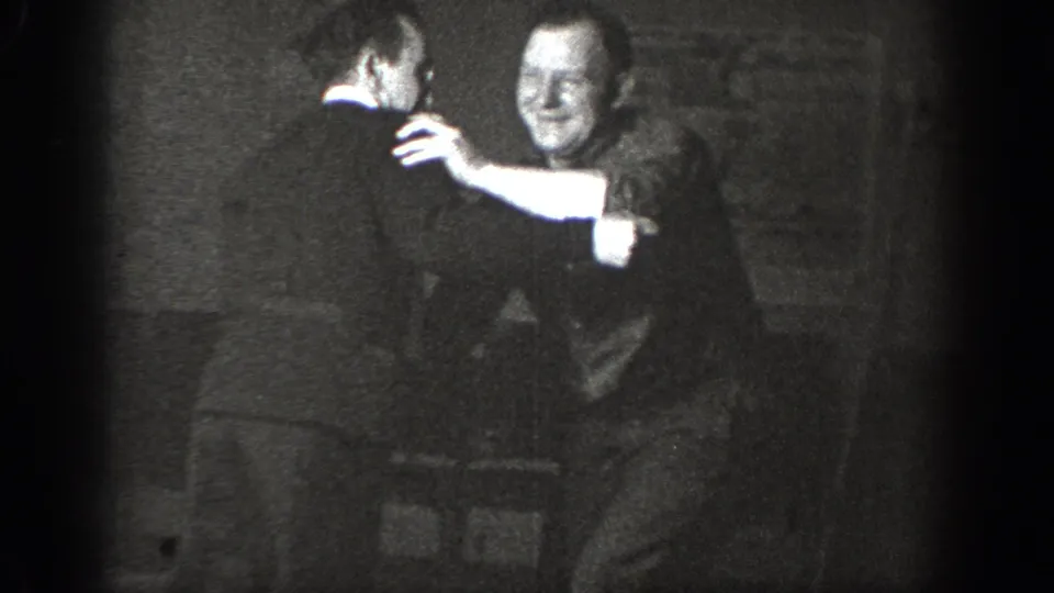 Grinning man faces camera during a physical struggle in a dark outdoor setting; the clearest frame of the clip, consistent with circa 1939 8mm home-movie footage.