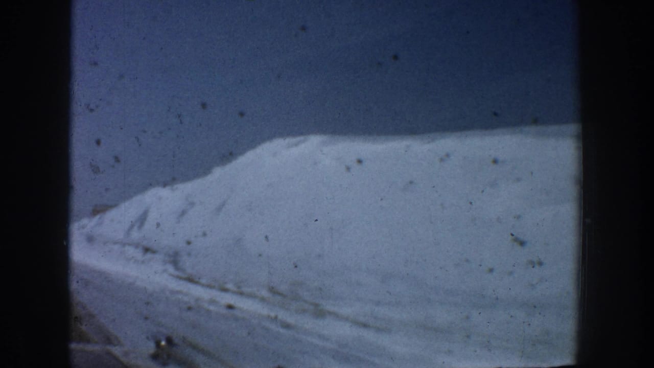 Close view of a towering roadside snowbank with textured, tracked surface against a deep blue sky, shot from a moving vehicle in Aspen, Colorado, circa 1961.