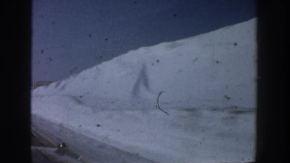 Roadside snowbank at road level on a winter drive, likely the Aspen, Colorado area circa 1961; a visible emulsion scratch and film hair cross the lower frame.