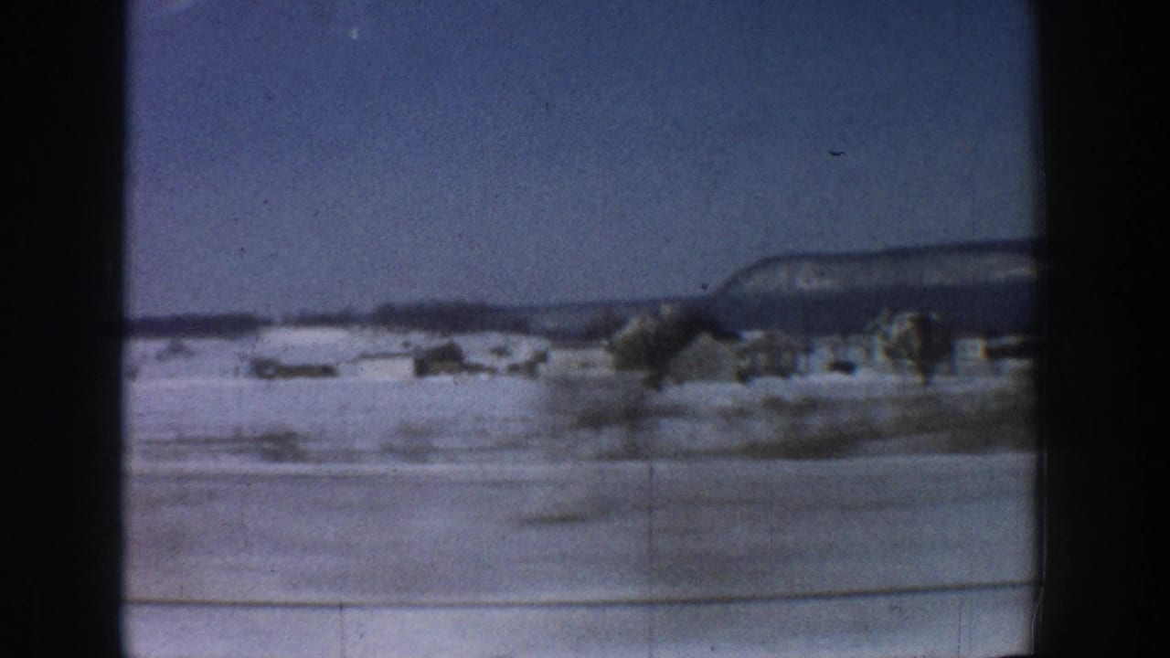 View through a car window across a snow-covered flat landscape with a distant flat-topped mesa under blue sky.