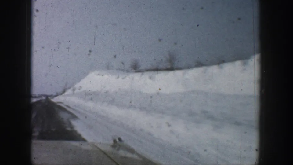 8mm shot through a car window showing a cleared road with high snow banks, consistent with a winter mountain drive in Colorado circa 1961.
