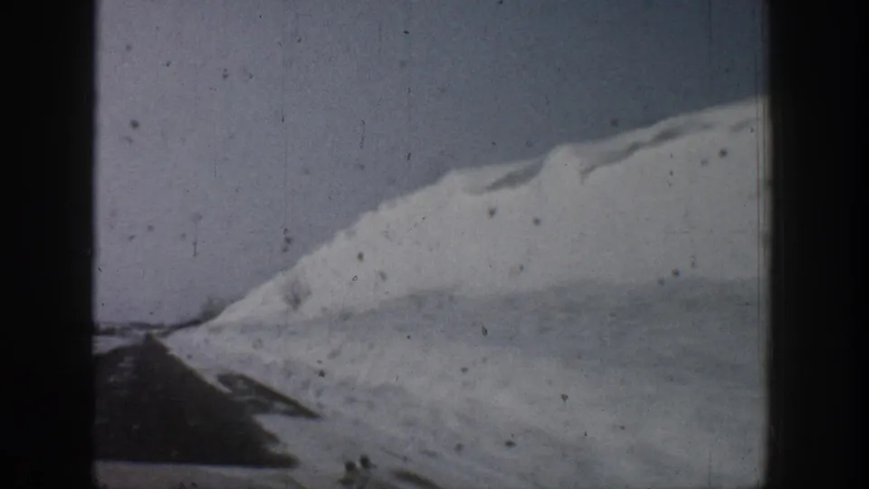 8mm road shot from inside a moving vehicle showing substantial snow drifts alongside a cleared winter road, consistent with a 1961 Colorado mountain drive.