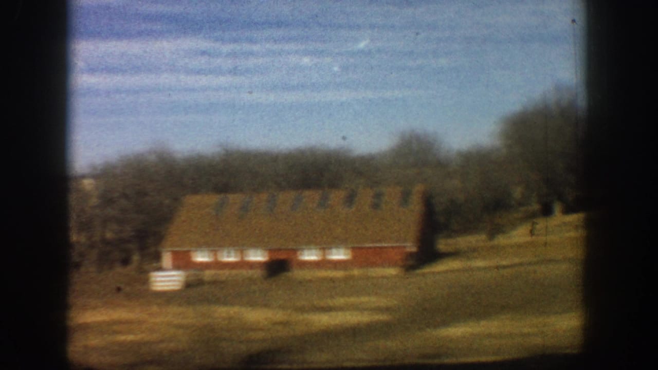 Red barn amid bare winter trees and dry golden fields, shot from a moving vehicle; 8mm home movie footage consistent with rural Colorado, 1961.