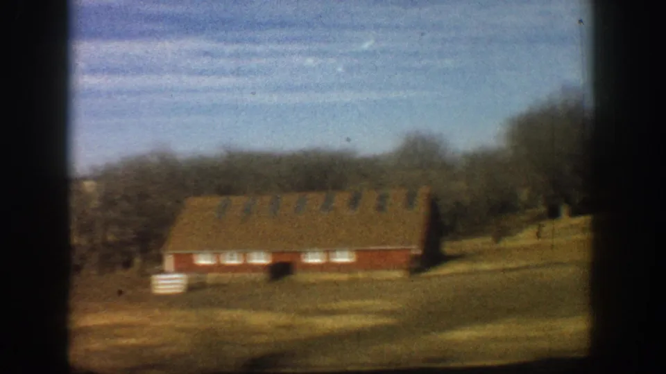 Red barn amid bare winter trees and dry golden fields, shot from a moving vehicle; 8mm home movie footage consistent with rural Colorado, 1961.