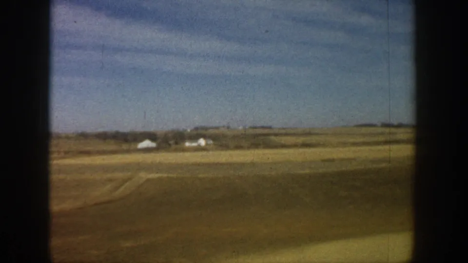 8mm home movie frame from a 1961 road trip showing vast flat plains with a white farmstead visible on the horizon.