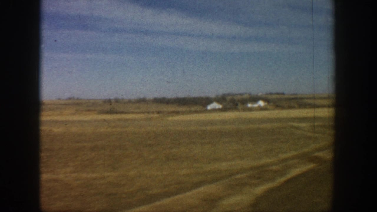 8mm travel footage circa 1961 showing treeless plains with white farmsteads on the distant horizon, viewed from a moving vehicle.