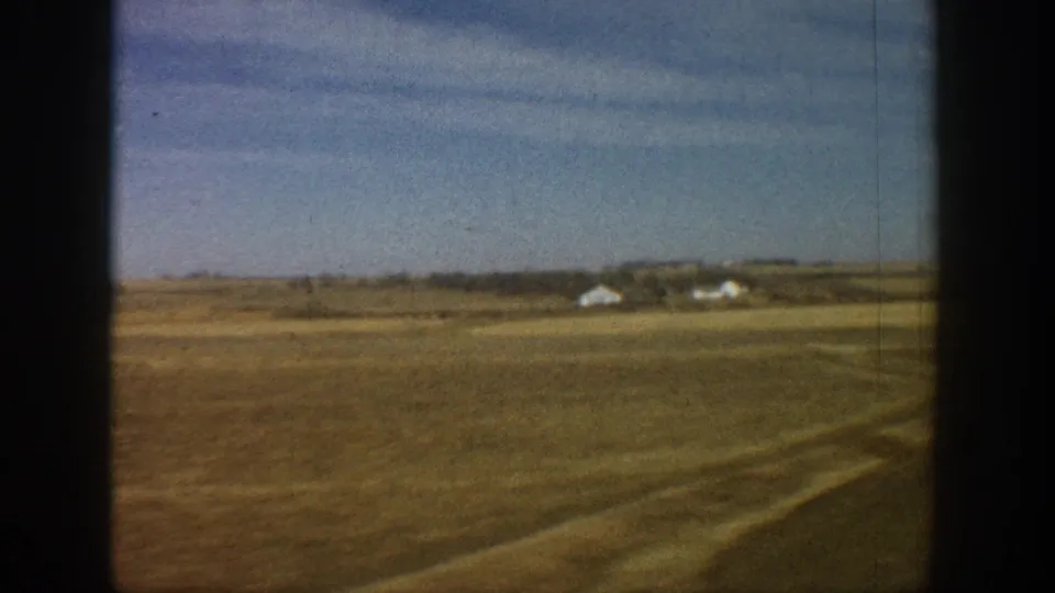 8mm travel footage circa 1961 showing treeless plains with white farmsteads on the distant horizon, viewed from a moving vehicle.