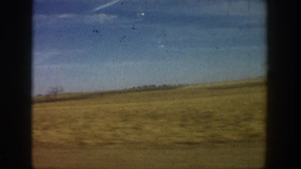 8mm home movie frame circa 1961 showing open dry Colorado prairie under blue sky with sparse horizon vegetation and visible film dust artifacts.