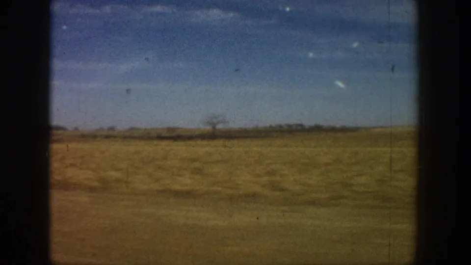 8mm home movie frame circa 1961 showing dry golden prairie and a low horizon line with sparse vegetation under a broad blue sky.