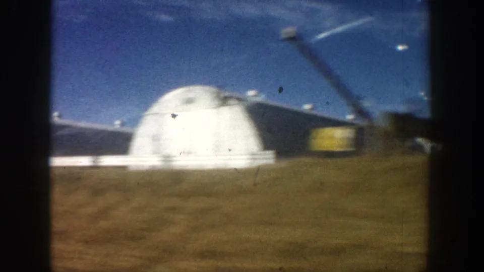 8mm home movie frame circa 1961 showing a large white dome building in close view alongside a dark flat-roofed structure, with an unidentified yellow element at frame edge, Colorado region.