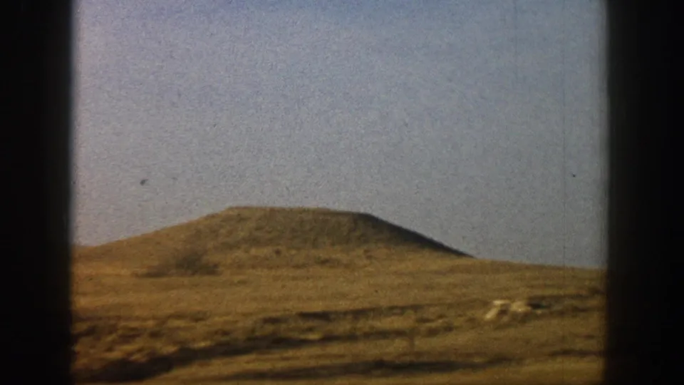 8mm home movie frame of low rounded hills with dry golden-brown grass, shot through vehicle window, reportedly Colorado, circa 1961.