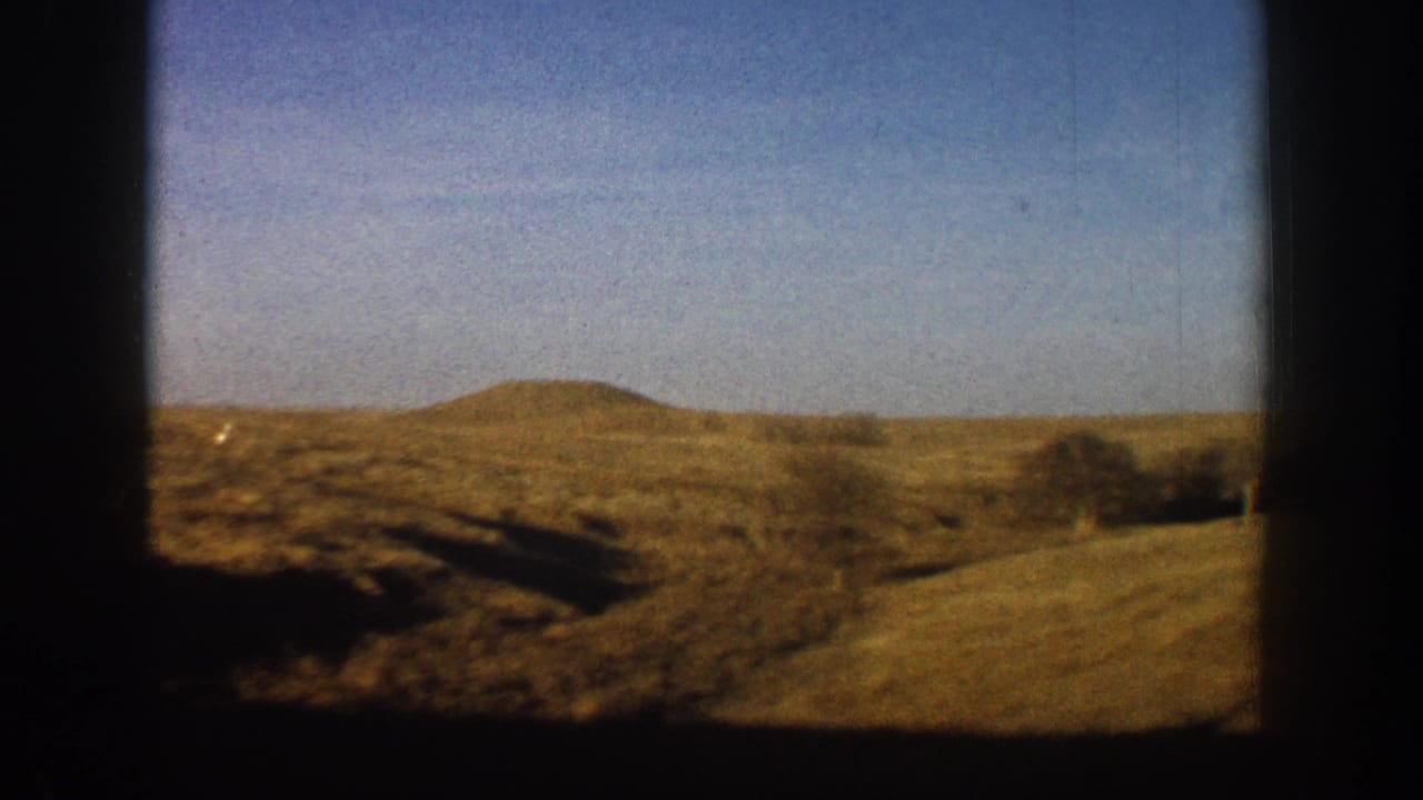 Low rounded hills with dry scrub vegetation filmed from a moving vehicle, consistent with early 1960s 8mm footage in Colorado's high desert terrain.