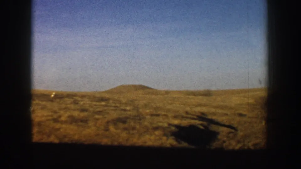 Open dry Colorado grassland with a solitary low hill on the horizon, filmed from a moving vehicle in what metadata dates to 1961 near Aspen.