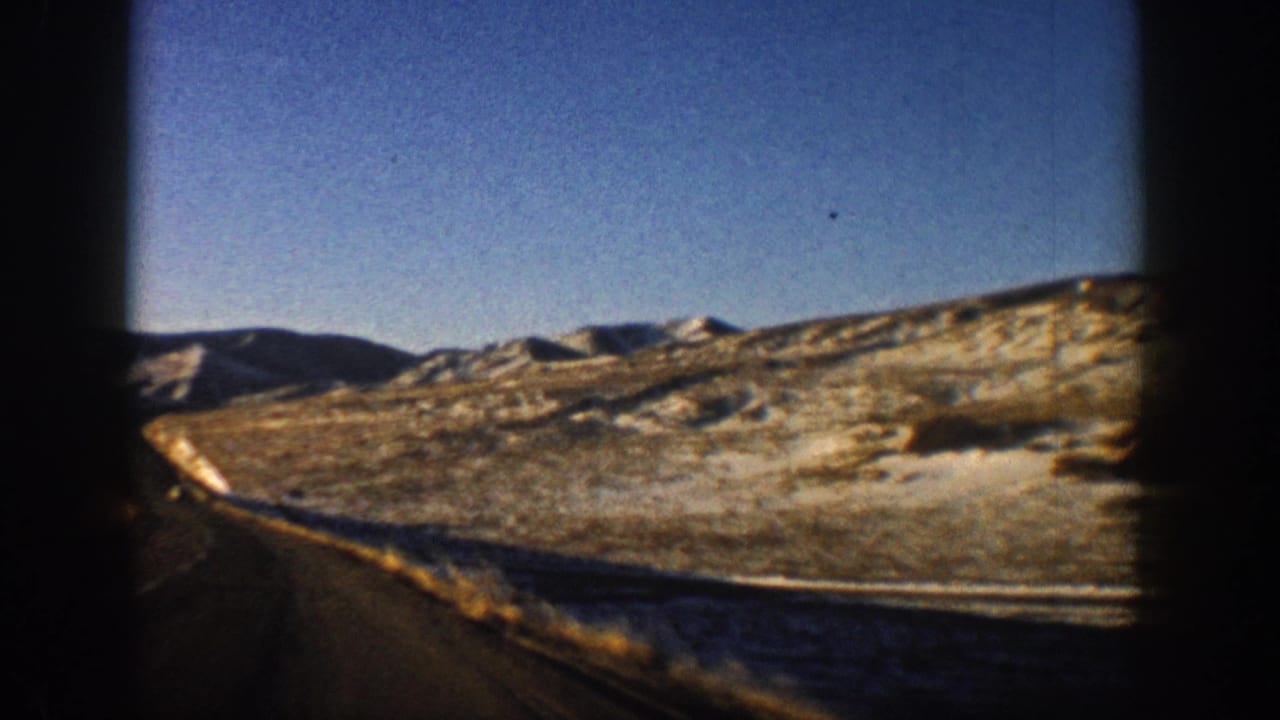 8mm film frame from a moving car showing a two-lane mountain road and brown, snow-dusted hillsides, Aspen, Colorado area, circa 1961.
