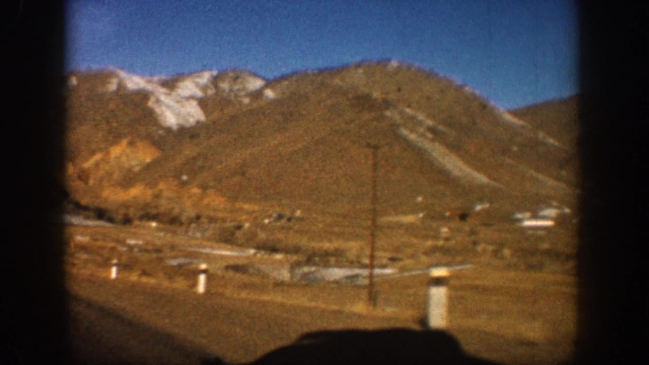 8mm home movie frame showing a rust-orange mountain with snow-dusted peak and a roadside utility pole, Colorado Rockies area, circa 1961.