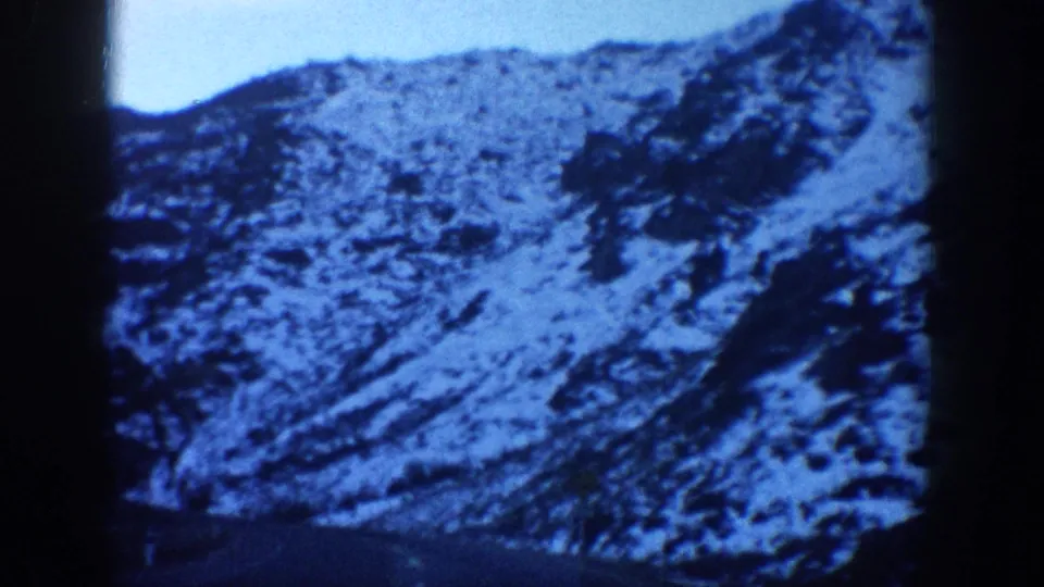 8mm home movie frame from the Aspen, Colorado area, circa 1961, showing a close pan across a snow-patched rocky mountain slope with blue sky at the top edge.