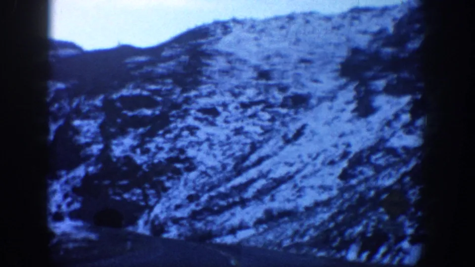8mm home movie frame from the Aspen, Colorado area, circa 1961, showing a wider valley view with snow-dusted slopes and a pale, blue-shifted sky.