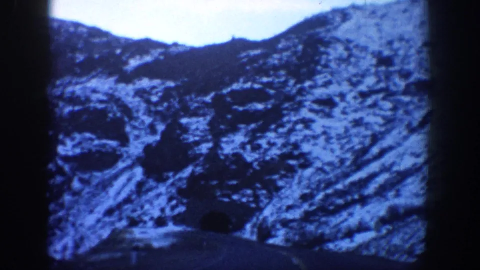 8mm home movie frame from the Aspen, Colorado area, circa 1961, showing a rugged snow-and-rock mountain face with heavy blue cast and coarse film grain.