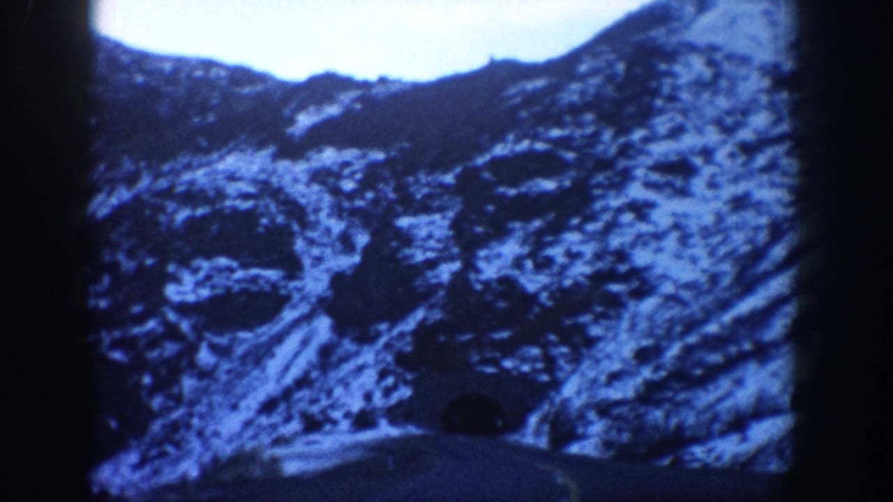 Blue-shifted 8mm view of a rugged, snow-patched mountain face in the Colorado Rockies, circa 1961, shot from a moving vehicle