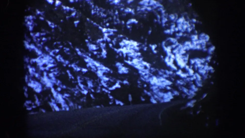 Blue-shifted 8mm close view of a snow-covered Rocky Mountain face with a dark road edge at the lower frame, circa 1961 Aspen area, Colorado