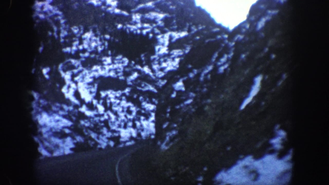 Snow-dusted rocky canyon walls shot from inside a moving vehicle, consistent with 1961 8mm home-movie footage from a Colorado mountain pass.