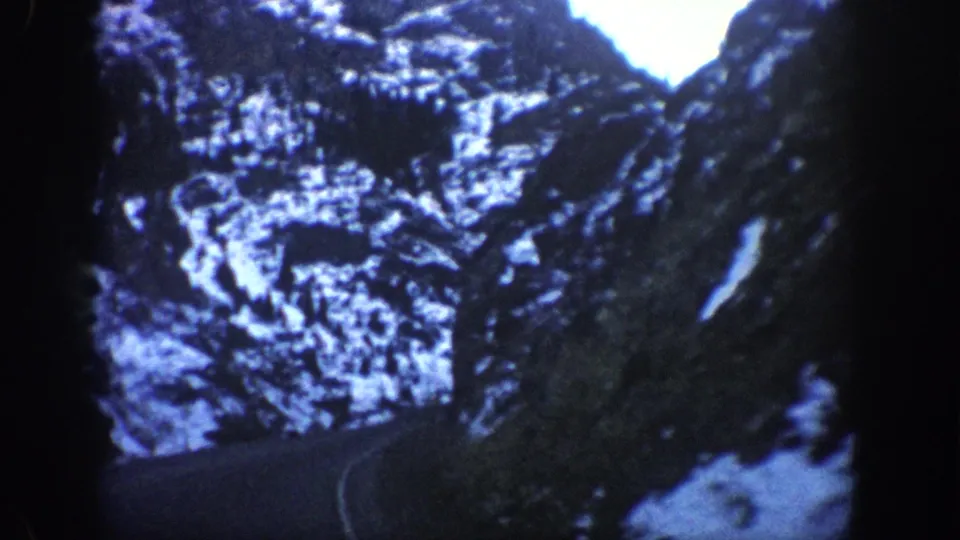 Snow-dusted rocky canyon walls shot from inside a moving vehicle, consistent with 1961 8mm home-movie footage from a Colorado mountain pass.