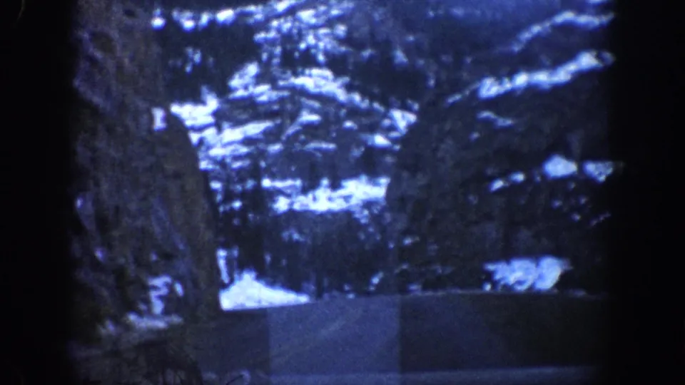 8mm frame of rugged snow-covered mountain terrain from a moving vehicle in winter, consistent with the Colorado Rockies circa 1961, with heavy film grain throughout.