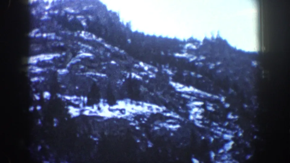 Snow-patched rocky canyon hillside with conifer trees and pale sky, Colorado Rockies area, circa 1961; characteristic 1960s 8mm blue cast.
