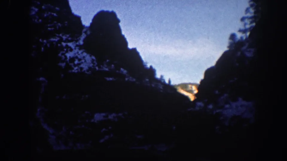 Silhouetted rock spires with warm amber light and blue sky in a Colorado canyon, circa 1961; snow visible on rock faces and surrounding slopes.