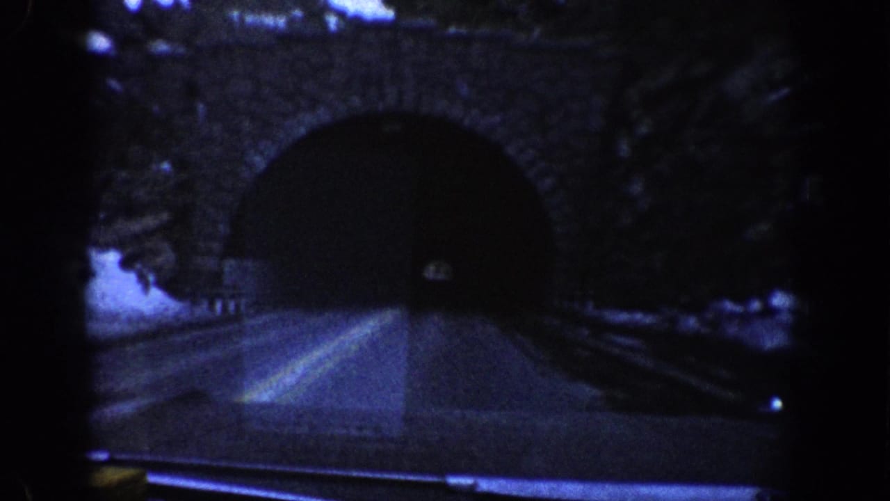 Stone-arch tunnel entrance with road lane markings, shot from a moving vehicle through the windshield.