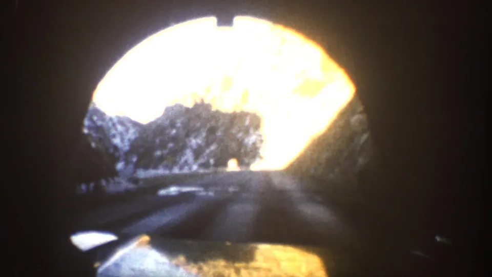 8mm home movie frame from inside a dark tunnel or enclosed space, showing a bright circular opening revealing a mountain canyon road, Colorado circa 1961.