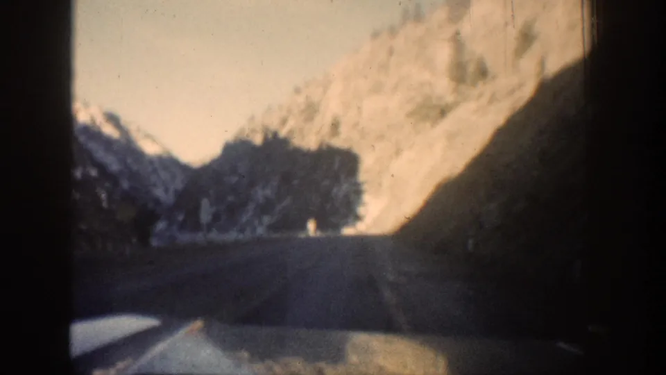 8mm road-level POV from inside a moving vehicle traveling through a rocky mountain canyon, likely Clear Creek Canyon, Colorado, circa 1961, snow visible on cliff faces.