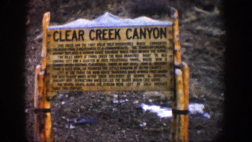 8mm close-up of the 'Clear Creek Canyon' wooden interpretive sign on aged timber posts, snow patches visible on rocky ground, Colorado circa 1961.