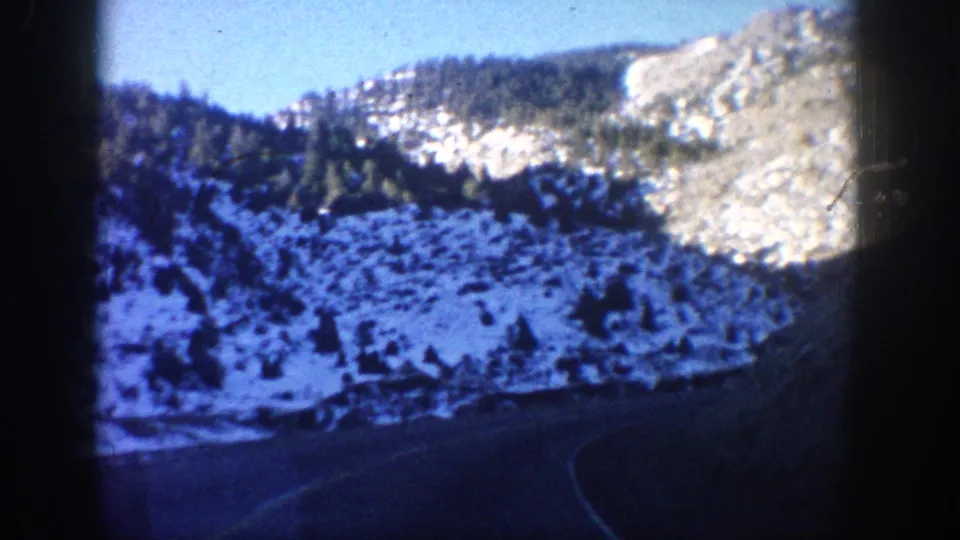Clear Creek Canyon, Colorado, circa 1961, snow-dusted rocky canyon walls, conifer forest on lower slopes, and a paved highway curving into the canyon, shot on 8mm from a moving vehicle.