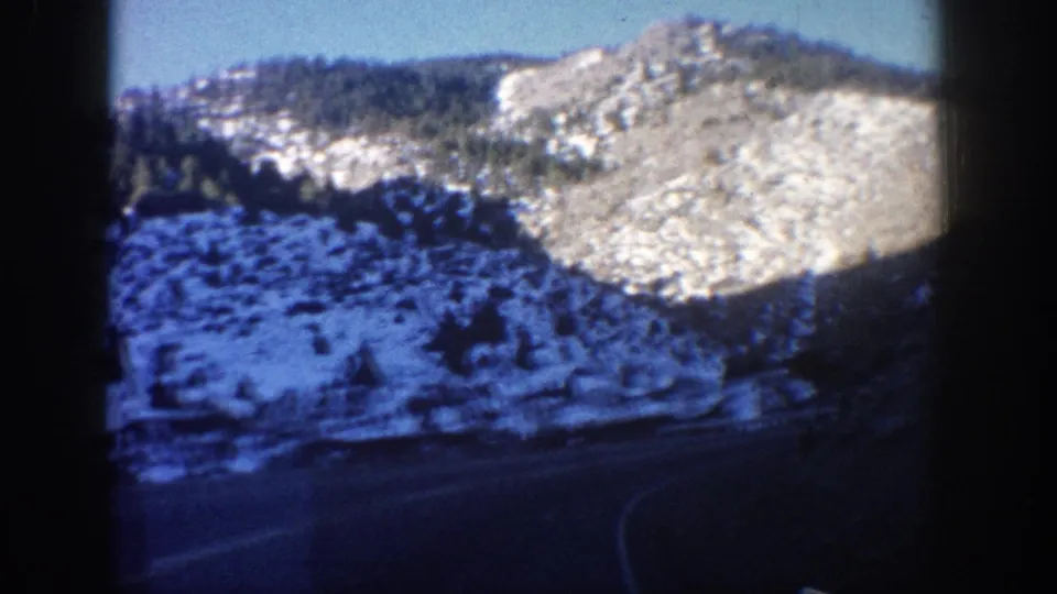 Clear Creek Canyon, Colorado, circa 1961, sunlit rocky cliffs with snow patches, coniferous forest, and a highway curve filmed on 8mm stock, likely through a vehicle window.
