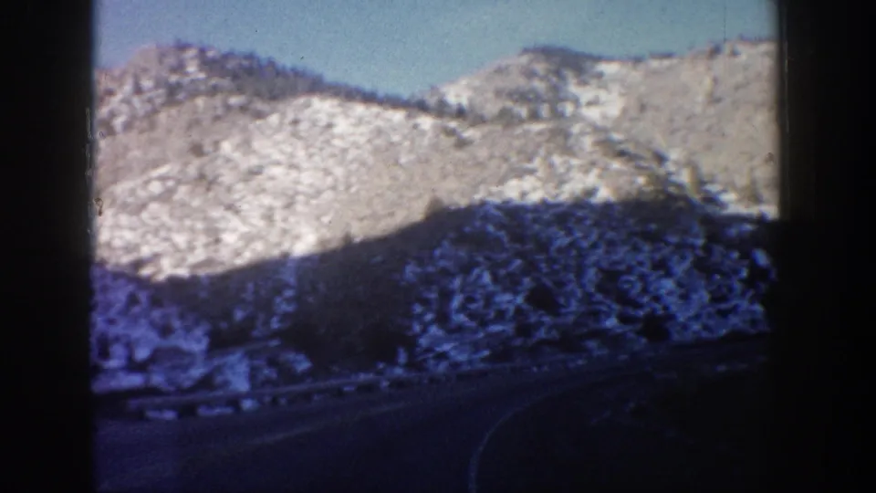 8mm footage of a snow-dusted mountain ridge near Aspen, Colorado, circa 1961, viewed from a moving vehicle with dark window vignetting.