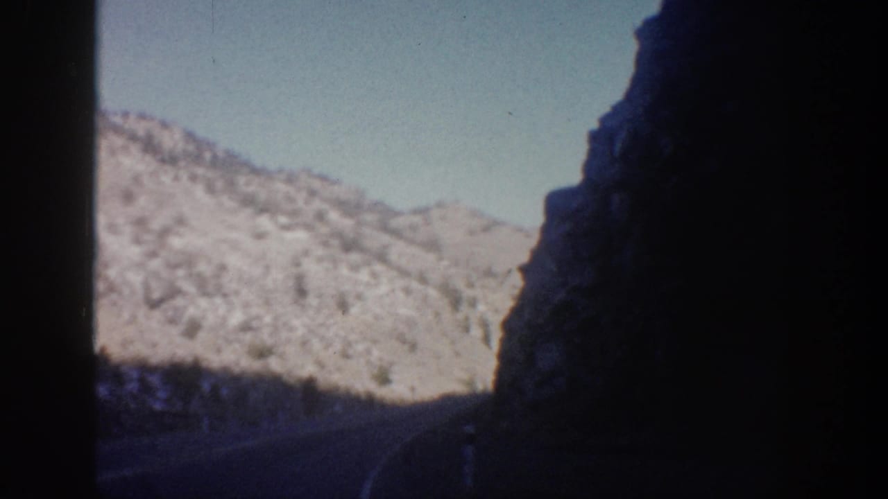 Curving mountain road bordered by dark rock walls and sunlit snowy hills.