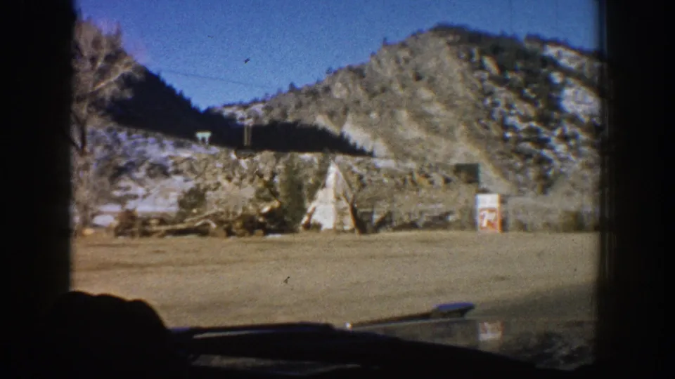 8mm film frame showing two roadside teepee structures, likely a tourist attraction, along a Colorado highway near Aspen c. 1961, filmed from a passing vehicle.