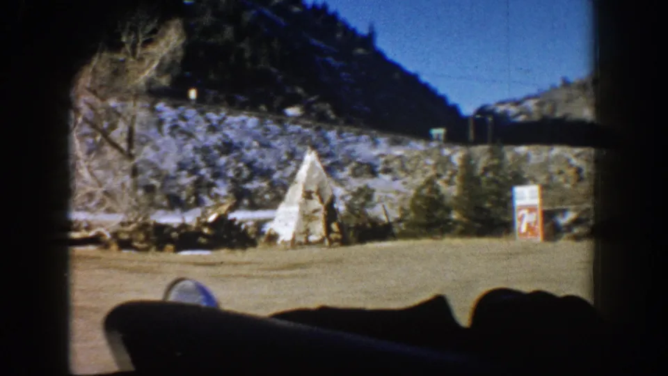 8mm home movie frame showing a roadside teepee attraction with possible commercial signage alongside a Colorado highway c. 1961, captured from a passing vehicle.