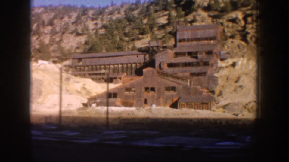 Multi-level weathered wooden mine mill building against rocky terrain with pine forest above, Aspen, Colorado area, circa 1961.