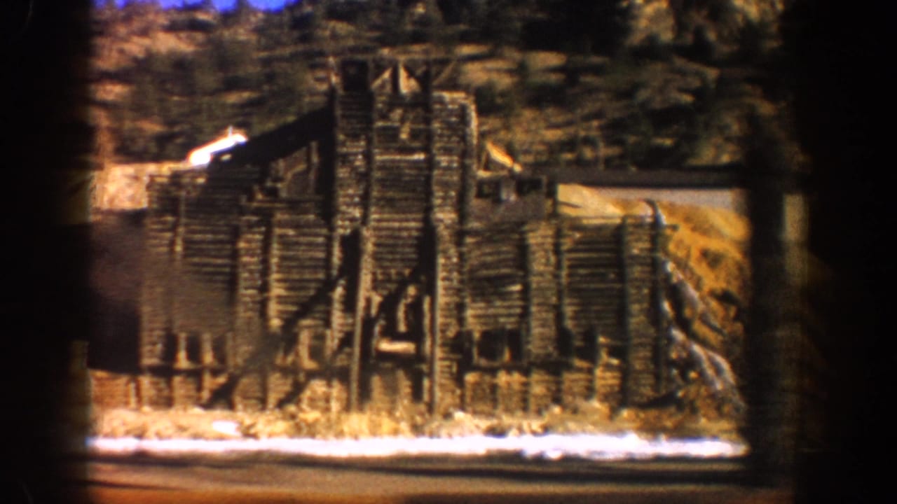 Dilapidated timber-frame structure, possibly a mine headframe or processing building, filmed from a moving vehicle in Aspen, Colorado area, 1961.