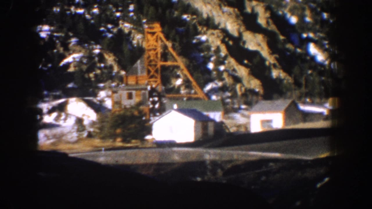 8mm frame from inside a vehicle showing an orange lattice-steel mine headframe, white cabin, and snow-patched mountain slopes, Aspen, Colorado area, 1961.