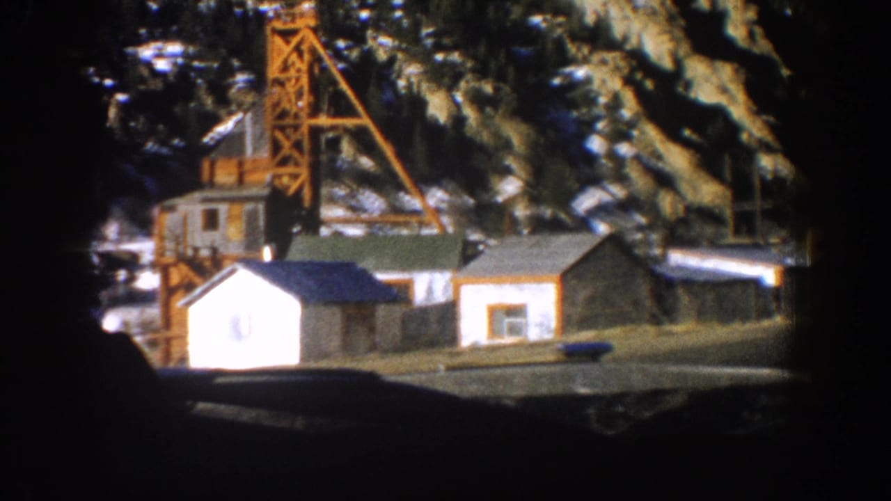 8mm frame showing a Colorado mine site with orange headframe, timber structures, and snow-dusted mountain backdrop, circa 1961.