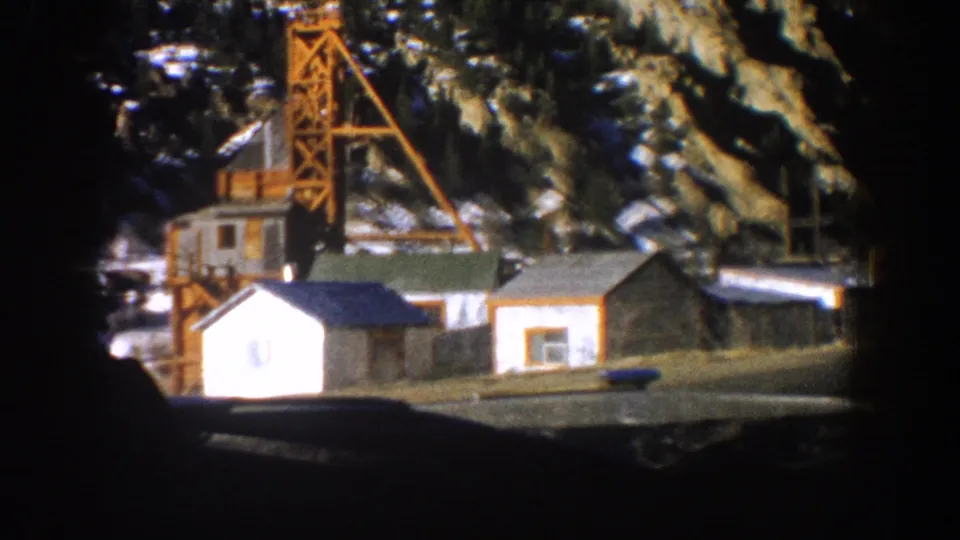 8mm frame showing a Colorado mine site with orange headframe, timber structures, and snow-dusted mountain backdrop, circa 1961.