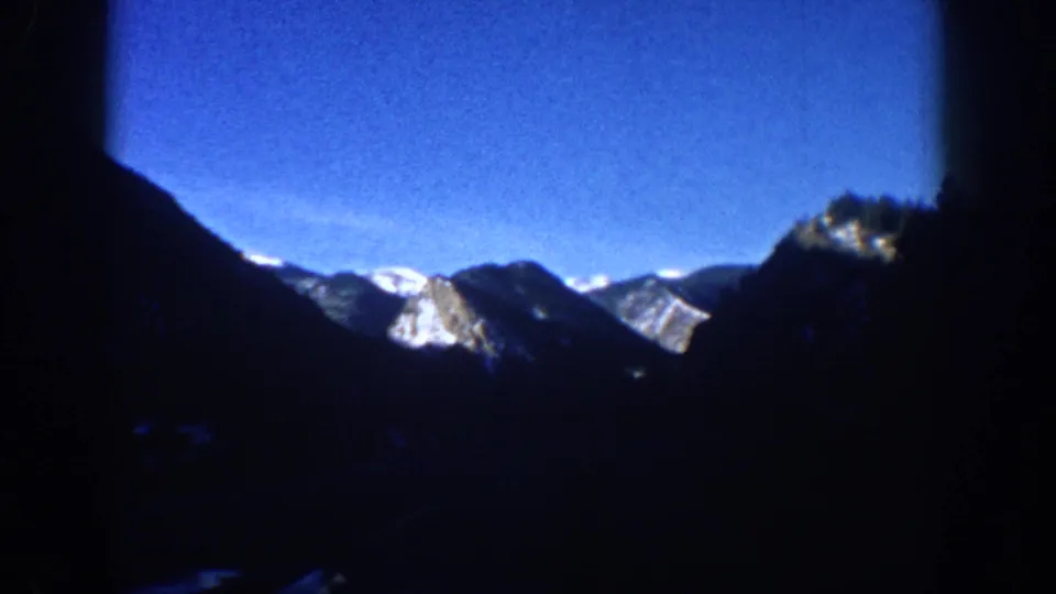 End-of-clip view of snow-covered Rocky Mountain peaks from a moving car, likely the Aspen, Colorado area, circa 1961; dark ridgeline silhouette in the foreground.