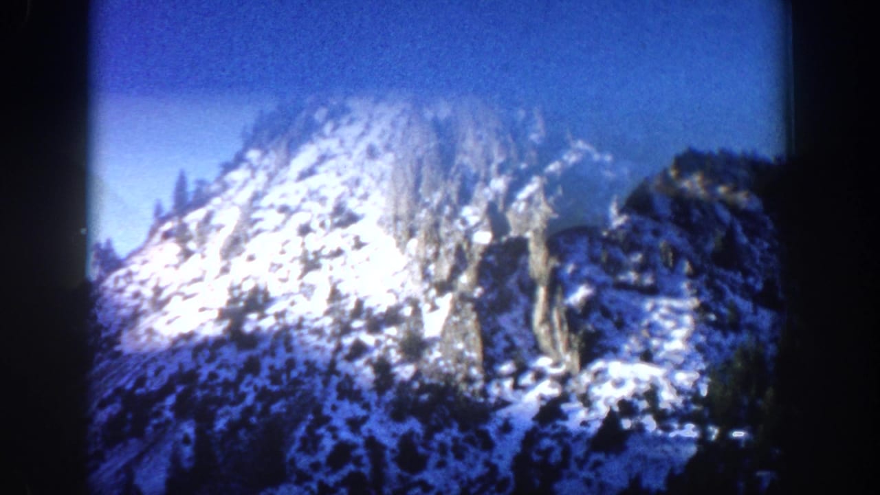 Close-up of a massive snow-covered rocky peak in strong sunlight, evergreen trees at lower edges, deep blue sky, 8mm vignette border.