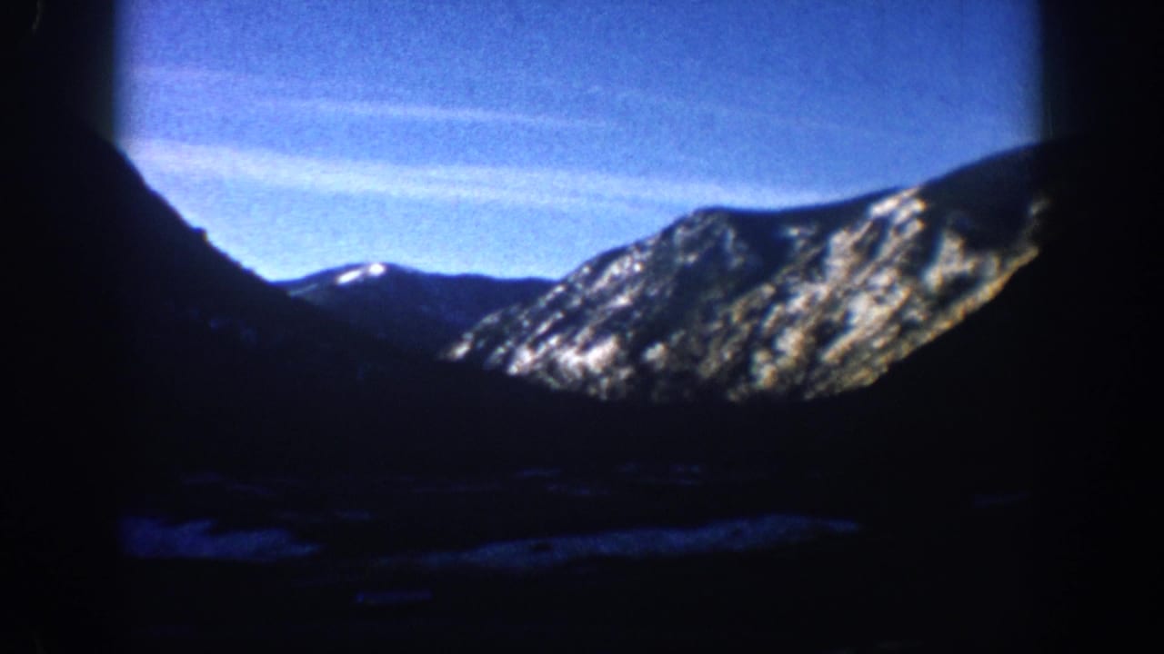 Wide 8mm view of snow-dusted Rocky Mountain peak and deep-shadow valley, vivid blue sky above, likely Aspen area Colorado circa 1961.