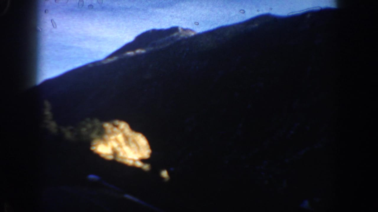 Close sunlit rock outcrop in warm amber tones against shadowed terrain and blue sky, Colorado Rockies area circa 1961, 8mm footage.