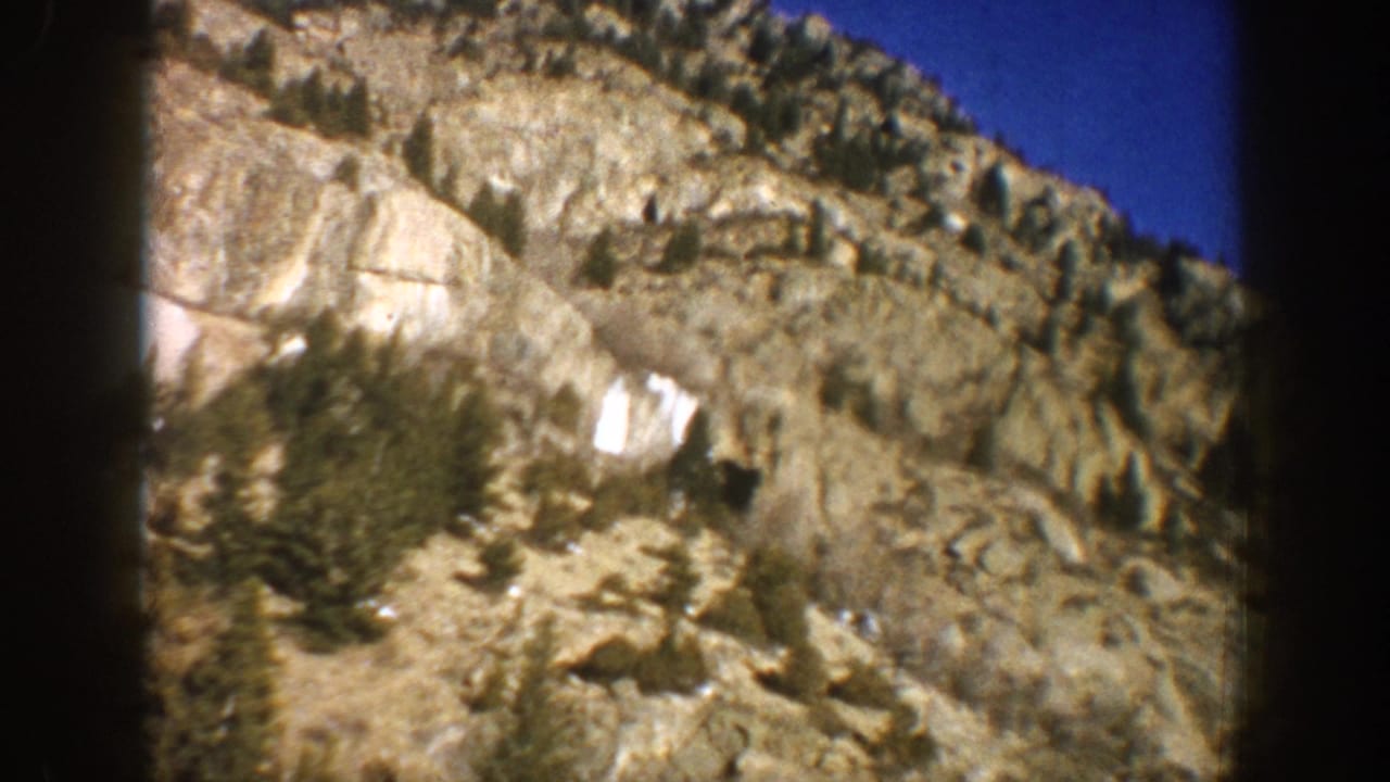 Close-up of steep rocky mountain slope with scattered conifers and snow patches shot on 8mm film, Aspen Colorado area, 1961