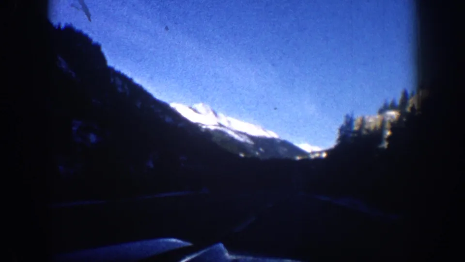 Wide mountain valley shot from inside a moving vehicle with snow-capped peaks visible in distance, Aspen Colorado area, 1961, 8mm film